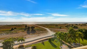 A coastal landscape with a paved walkway leading to the beach, surrounded by greenery and palm trees. - Treasure Island Beachfront-Top Floor End Unit  Stunning Sunsets South Beach 601 (Treasure Island)