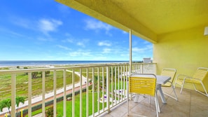 A balcony with a view of the beach and ocean, a table with chairs, and a yellow wall. - Treasure Island Beachfront-Top Floor End Unit Stunning Sunsets South Beach 601 (Treasure Island)