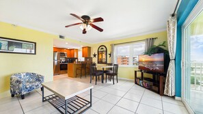 A modern kitchen with stainless steel appliances, a dining area with a table and chairs, a ceiling fan, and a large window with a view of the sea. - Treasure Island Beachfront-Top Floor End Unit  Stunning Sunsets South Beach 601 (Treasure Island)