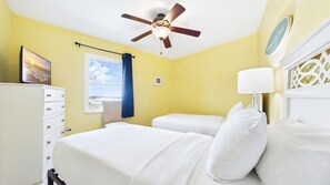 A hotel room with two beds, a ceiling fan, a window with a view, a dresser, and a bedside lamp. - Treasure Island Beachfront-Top Floor End Unit  Stunning Sunsets South Beach 601 (Treasure Island)