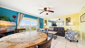 A dining area with a round table and chairs, a sofa, and a ceiling fan. - Treasure Island Beachfront-Top Floor End Unit  Stunning Sunsets South Beach 601 (Treasure Island)