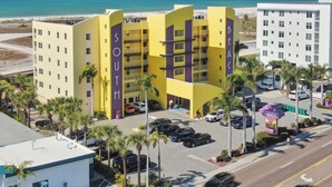 Un hotel de varios pisos con un cartel llamativo que dice 'SOUTH', zona de estacionamiento y vista a la playa.