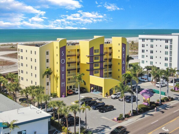 A multi-story hotel with a prominent 'SOUTH' sign, parking area, and a view of the beach. - Treasure Island Beachfront-Top Floor End Unit Stunning Sunsets South Beach 601 (Treasure Island)