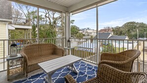 A covered balcony with wicker furniture, a table, and a view of a swimming pool and buildings. - Cottage Glyn - 3 BR Home Steps to the Beach (North Myrtle Beach)