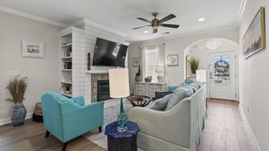A modern living room with a fireplace, teal sofas, and a television. - Cottage Glyn - 3 BR Home Steps to the Beach (North Myrtle Beach)