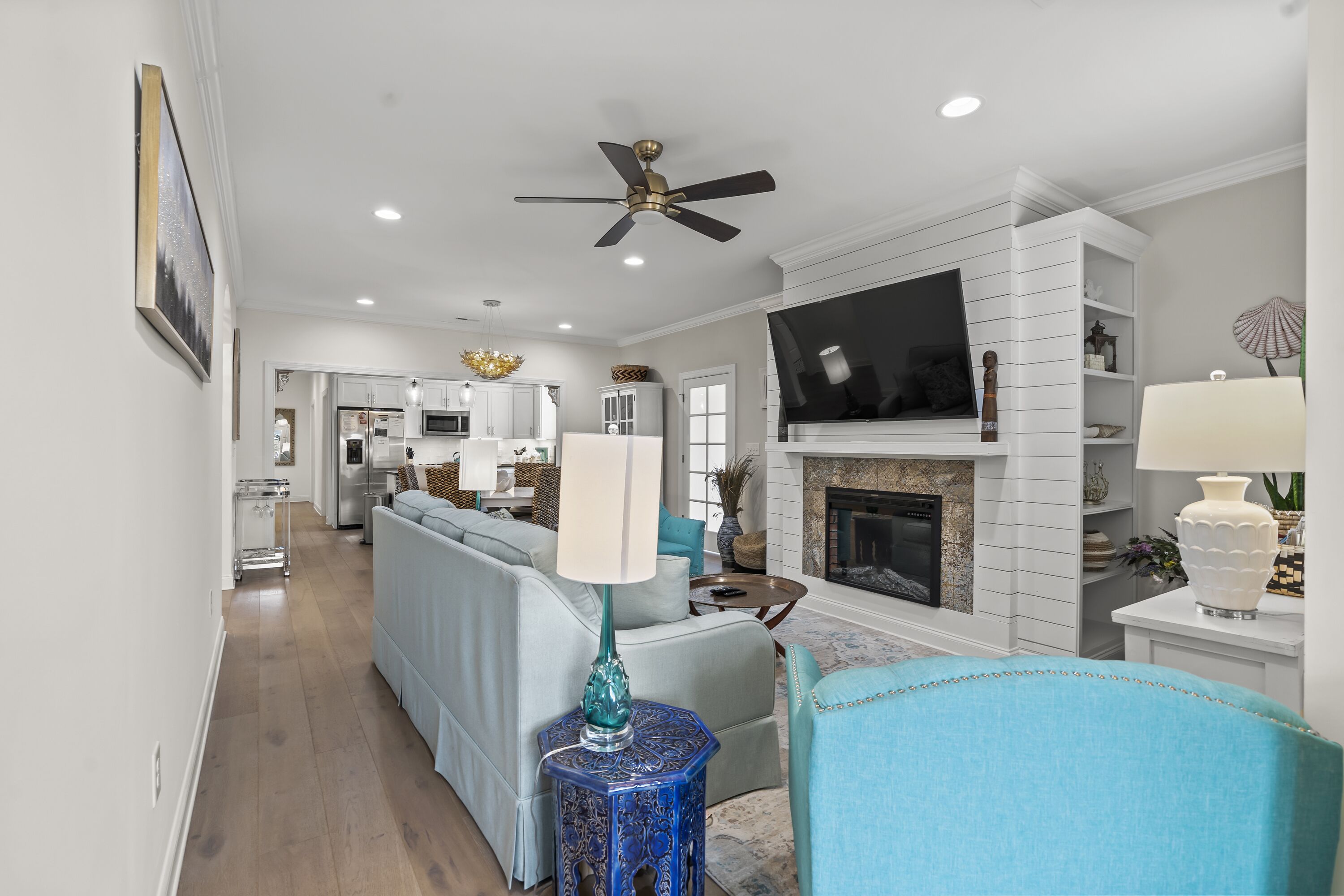 A modern living room with a sofa, a blue armchair, a fireplace, a television, and a ceiling fan.
