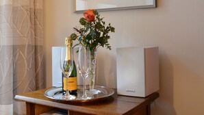 A wooden side table with a framed black and white photograph, a bottle of champagne, two wine glasses, a vase with a flower, and a white electronic device. - REISEKULTOUREN Apartment PAULINE in the center of Detmold (Detmold)