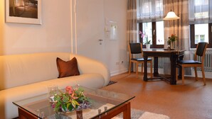 A living room with a sofa, a glass coffee table with a flower arrangement, a dining table with chairs, and large windows with curtains. - REISEKULTOUREN Apartment PAULINE in the center of Detmold (Detmold)