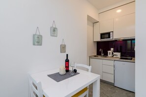 A compact kitchen with white cabinets, a microwave, and a toaster. There is a small dining table with a placemat, a wine bottle, and a candle.