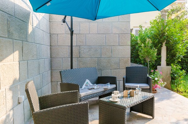 An outdoor patio with wicker furniture, a table, and a blue umbrella.