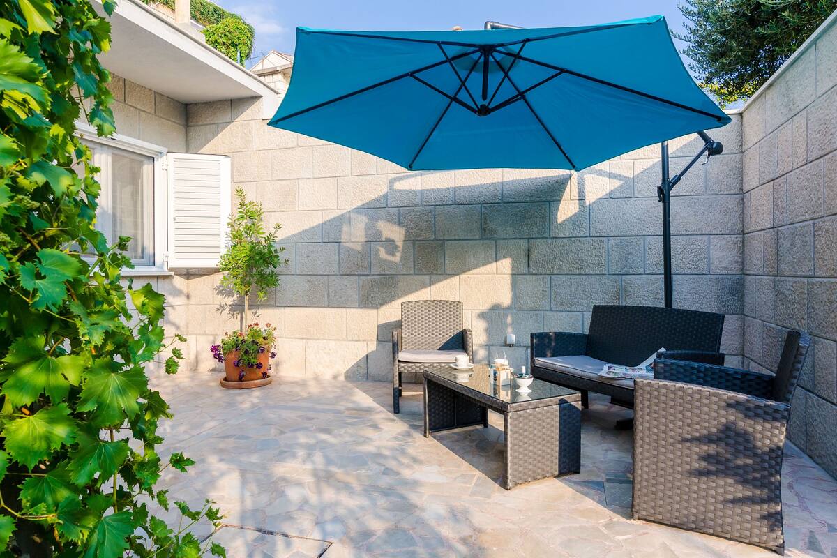 An outdoor patio with a blue umbrella, wicker furniture, and a potted plant.