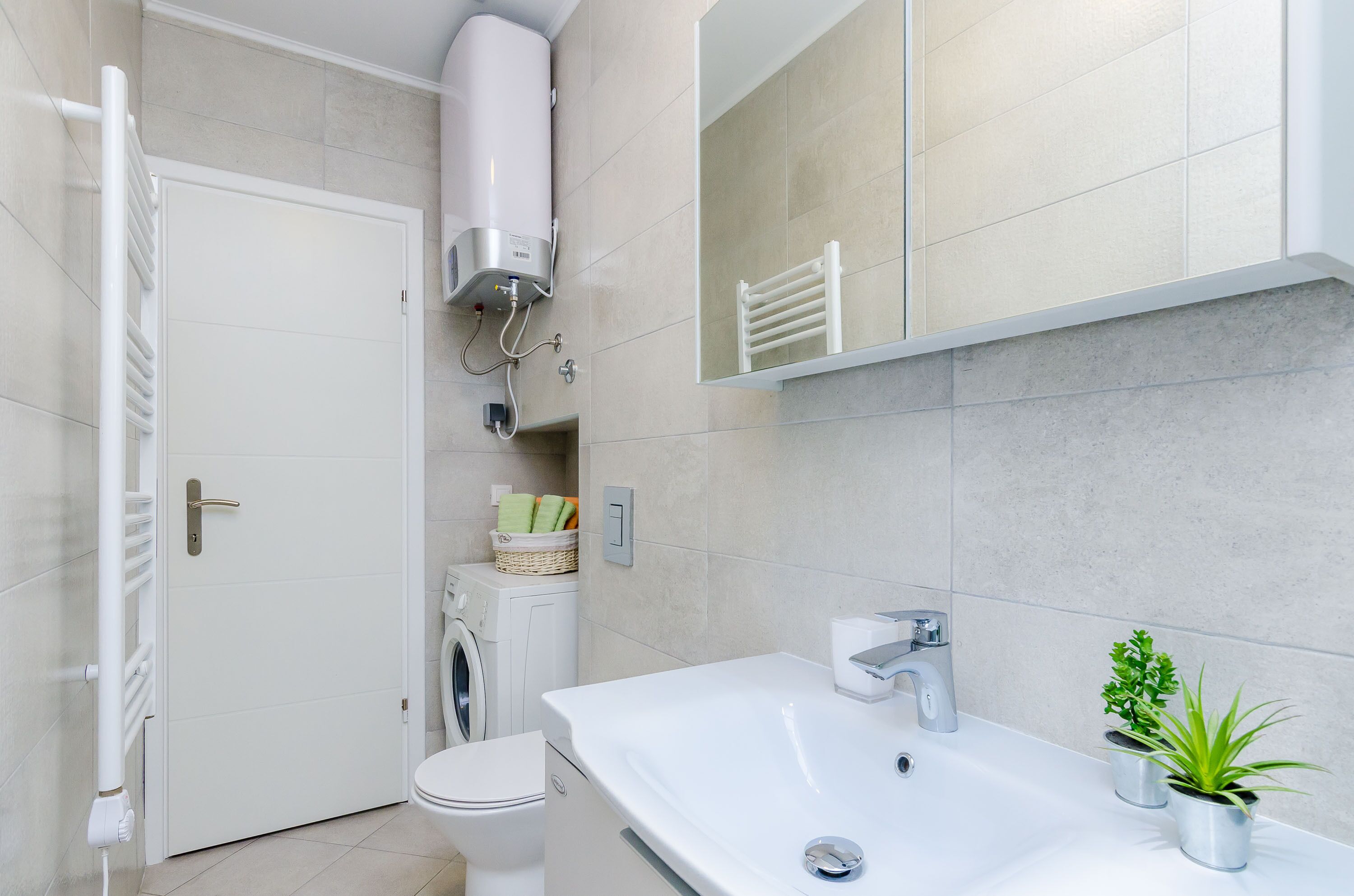 A modern bathroom with a white sink, a mirror, a towel rack, a washing machine, and a radiator.