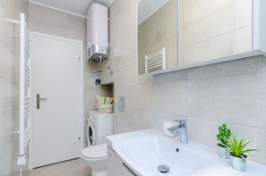 A modern bathroom with a white sink, a mirror, a towel rack, a washing machine, and a radiator.