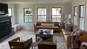 A living room with a fireplace, leather sofas, a coffee table, and large windows with views of greenery. - Fully Renovated In-Town Family-Friendly Home (Crested Butte)