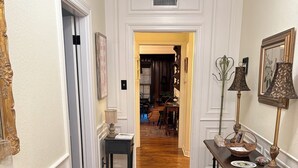 Un pasillo con piso de madera, un tapete estampado, una mesa con adornos y una puerta que da a otra habitación.