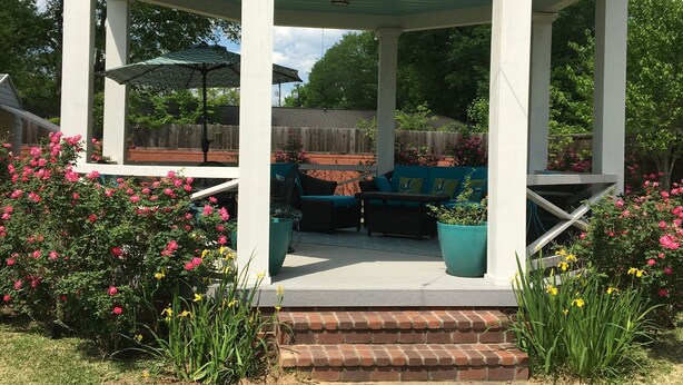 Un patio techado con un conjunto de asientos, un sendero de ladrillos y abundante vegetación.