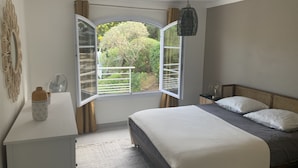 Une chambre avec un grand lit, une table de chevet, une fenêtre avec des rideaux et un luminaire suspendu.