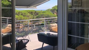 Un espace extérieur aménagé, abrité et doté de mobilier en osier, offrant une vue sur des arbres verdoyants et la mer.