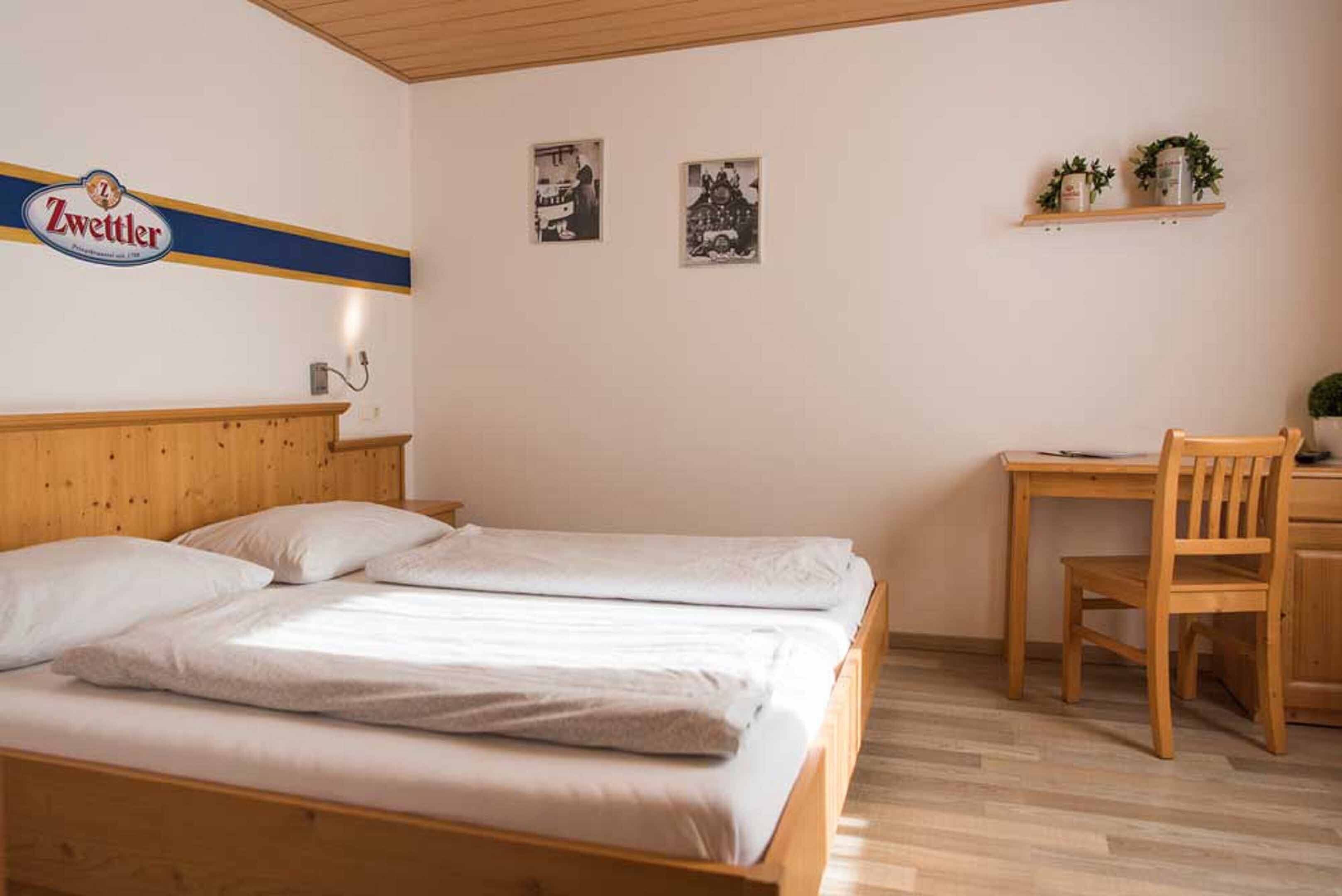 Een hotelkamer met een houten bed, een bureau en twee ingelijste foto's aan de muur.