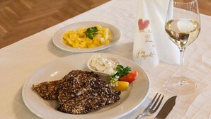 A meal consisting of a breaded cutlet, a bowl of potato salad, and a glass of white wine on a table with a white tablecloth.