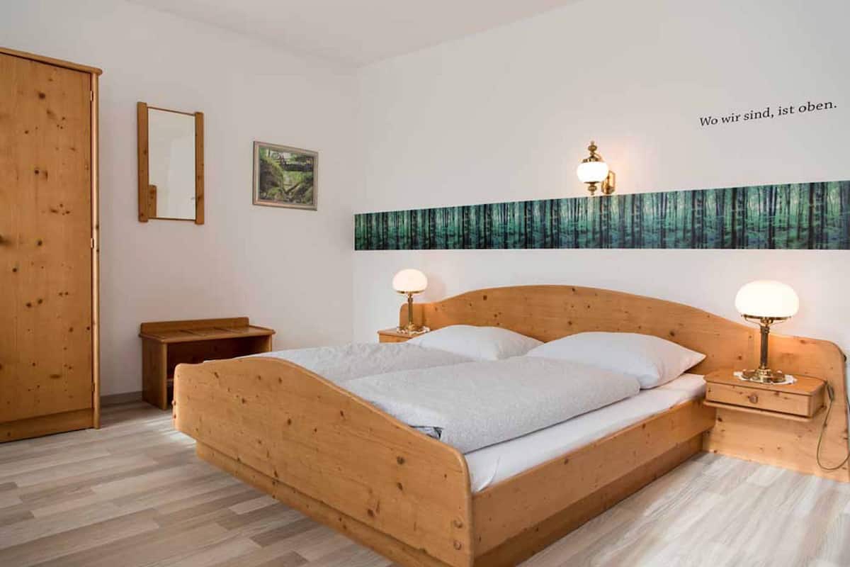 A wooden bed with two bedside tables, a mirror, and a wall-mounted light fixture.