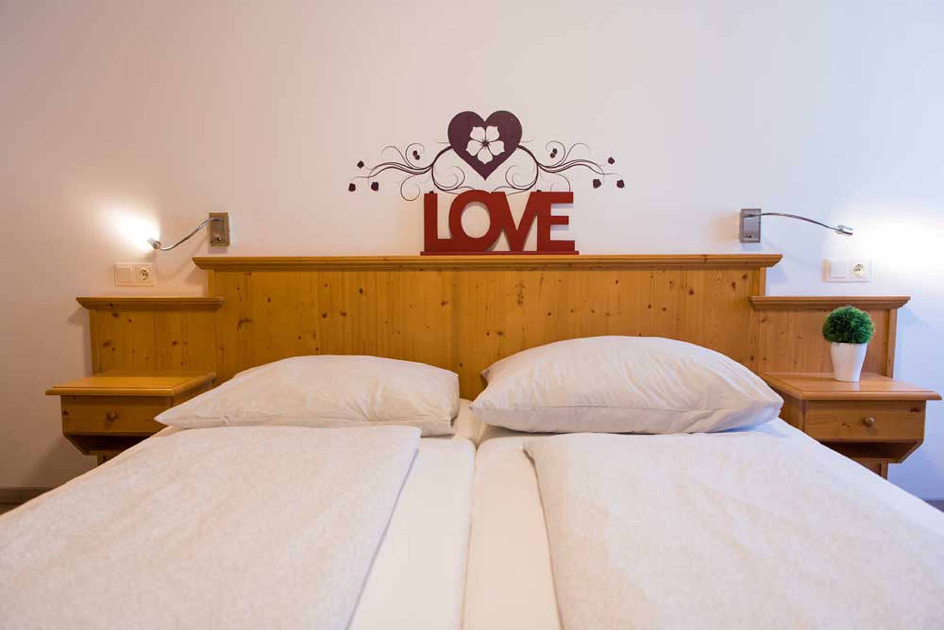 A double bed with a wooden headboard, two bedside tables, and a wall decoration with the word "LOVE" and a heart symbol.