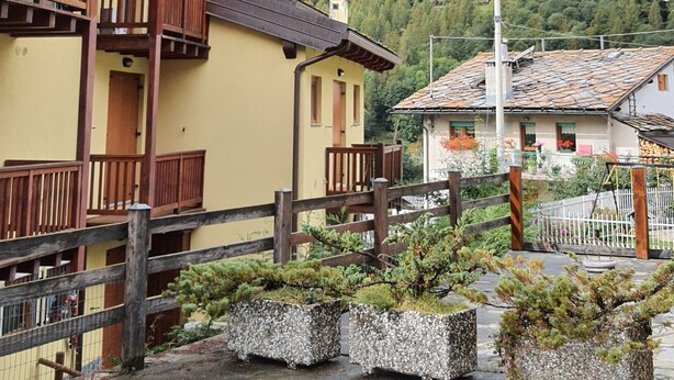 A mountain village with traditional wooden houses, a wooden fence, and a view of a forested mountain. - Sweet Home ski out (Valtournenche)