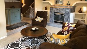 A living room with a fireplace, a sofa, a coffee table, and a staircase leading to another room. - Moden West Seattle House in the Trees (Seattle)