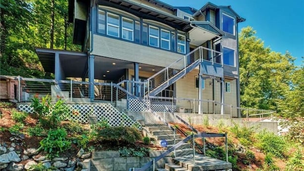 A modern two-story house with a covered porch, a staircase leading to the upper level, and a view of a forested area. - Moden West Seattle House in the Trees (Seattle)