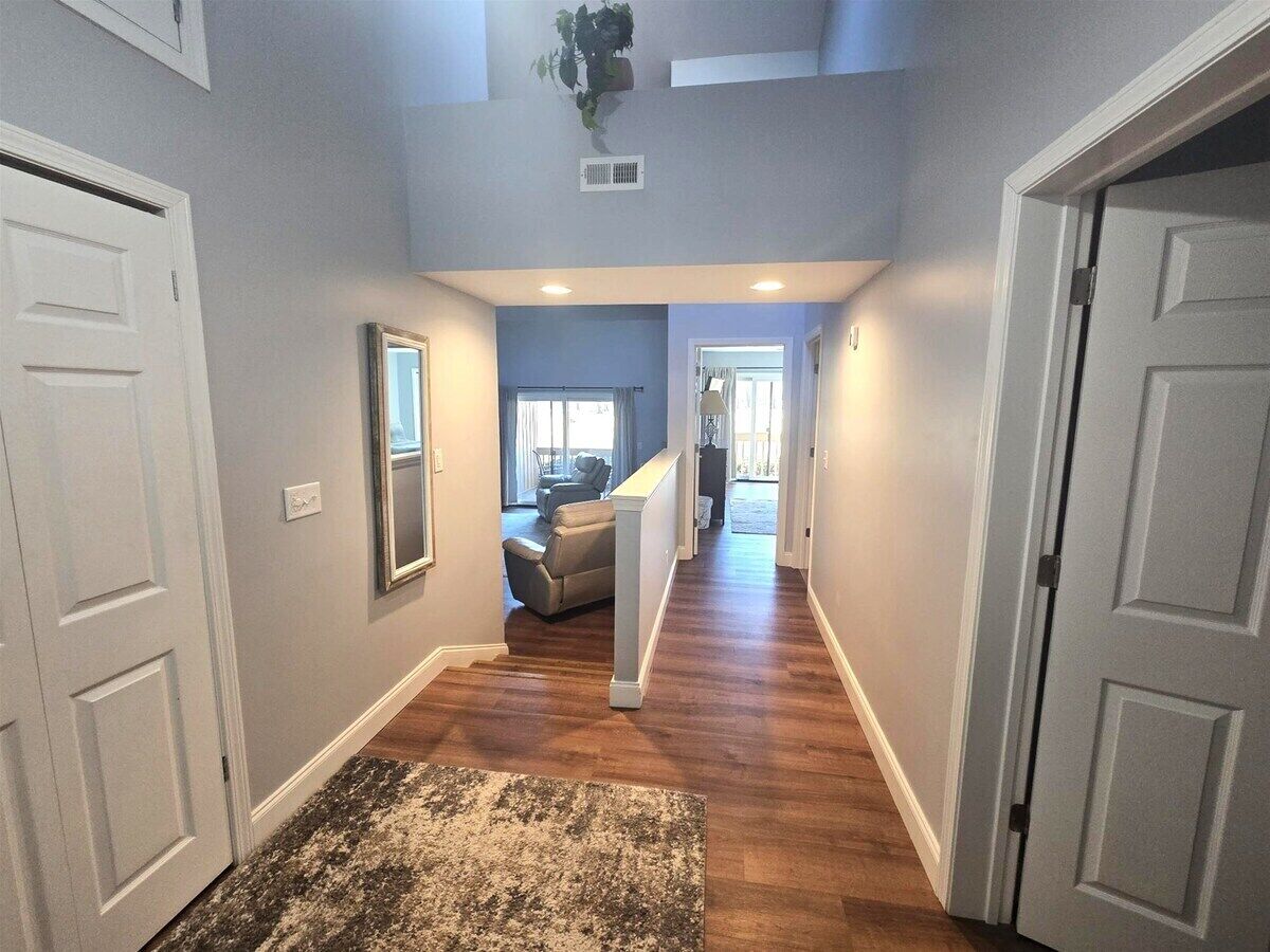 A hallway with wooden flooring, white doors, and a staircase leading to a living area.