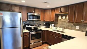 A modern kitchen with stainless steel appliances, wooden cabinets, and a stone backsplash.
