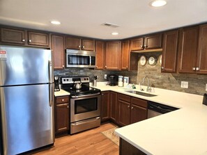 A modern kitchen with stainless steel appliances, wooden cabinets, and a stone backsplash. - Fairway Villa 1501 at Rumbling Bald (Lake Lure)