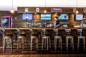 A bar area with wooden bar counters, multiple stools, and a variety of bottles and glasses.
