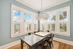 A dining room with a table, chairs, a chandelier, and large windows with shutters. - Seagrove House, Saltwater Pool, Gulf and Lake Views, Screened Porch, Steps to Be (Santa Rosa Beach)