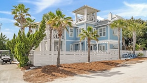 A large, two-story house with a white fence, palm trees, and a bicycle.