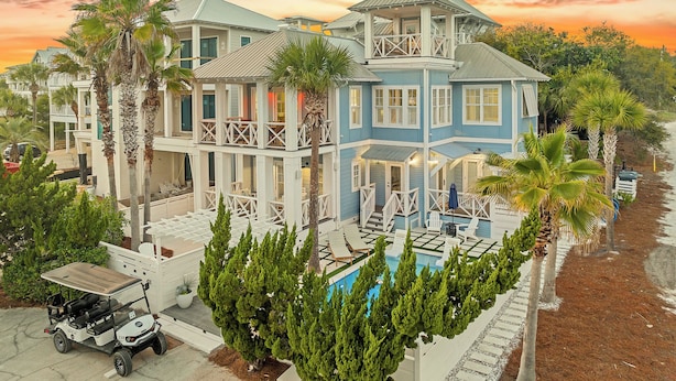 A multi-story house with a pool, surrounded by palm trees and a golf cart.