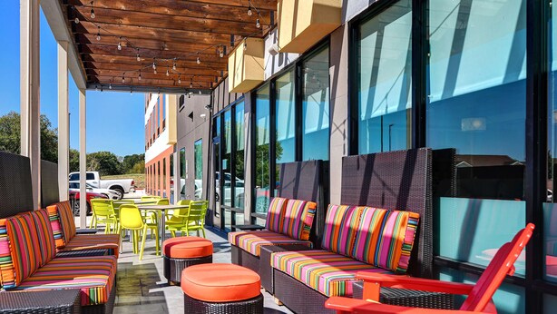 Un área de estar al aire libre con muebles de mimbre, cojines coloridos, ventanas amplias y una pérgola de madera.