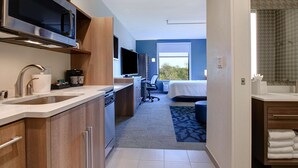 Una habitación de hotel moderna con zona de cocina, un ventanal grande y vistas a árboles.