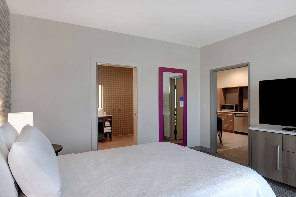 Habitación de hotel con cama, televisión, escritorio y kitchenette.