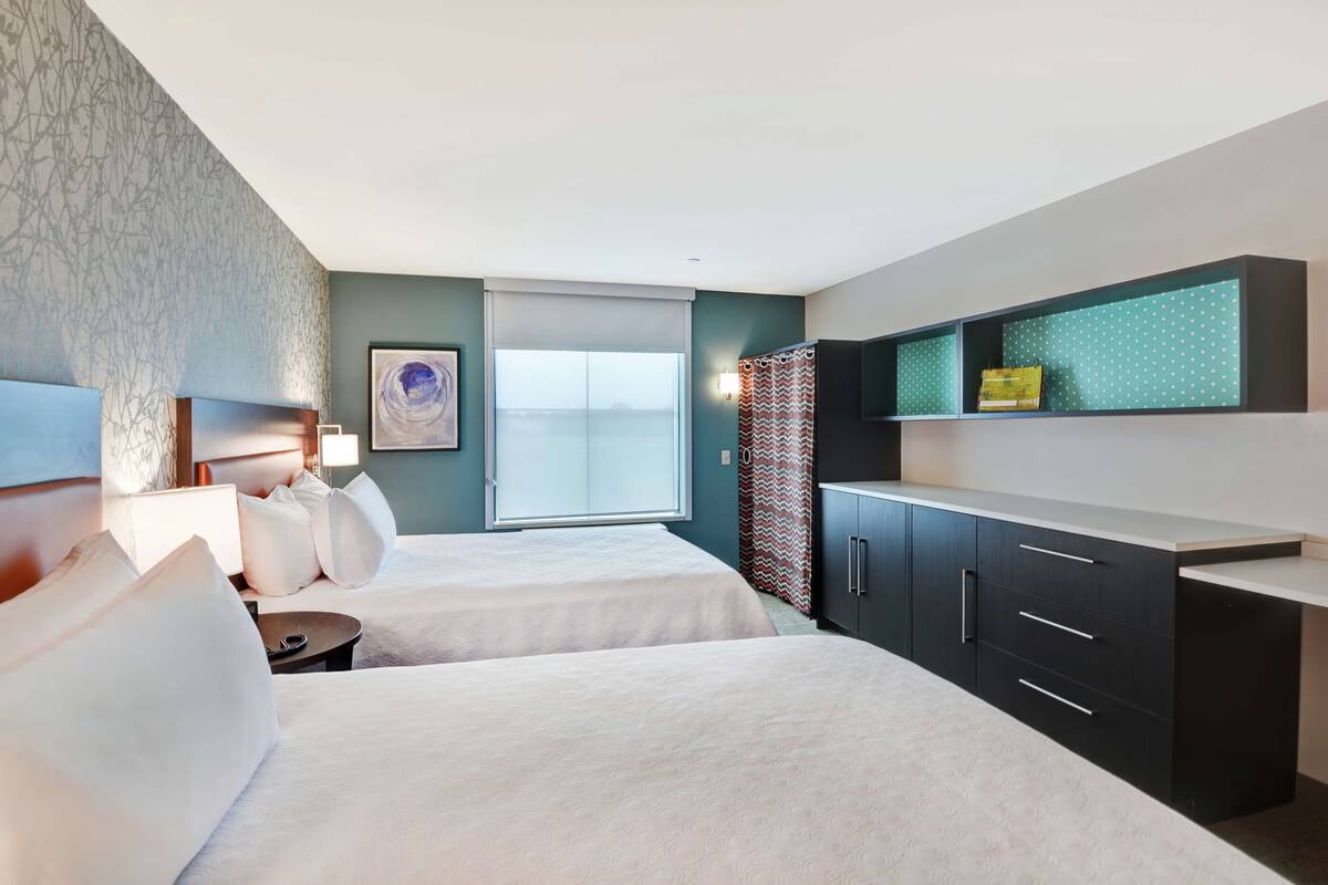 Habitación de hotel con dos camas, un escritorio, un televisor y una ventana con vistas.
