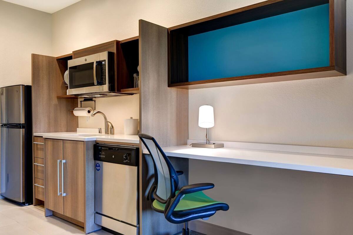 Cocina compacta con microondas, refrigerador, lavavajillas y una silla.