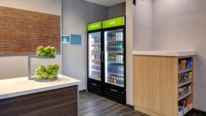 Una zona de kitchenette con dos refrigeradores, un frutero y un letrero que dice 'HOME 2 MKT'.