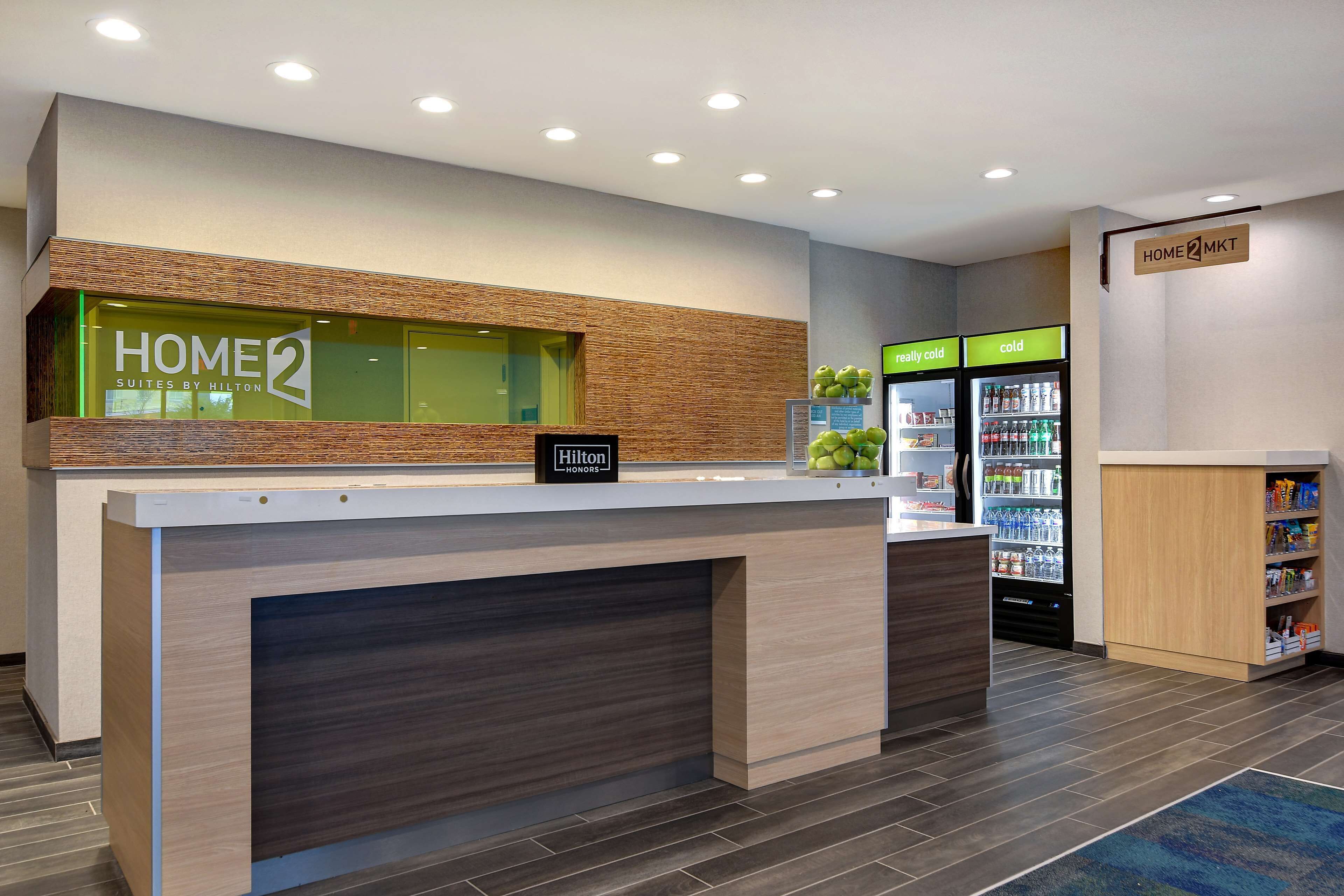 A hotel reception area with a modern design, including a reception desk, a minibar, and a refrigerator stocked with beverages.