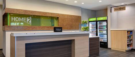 A hotel reception area with a modern design, including a reception desk, a minibar, and a refrigerator stocked with beverages.