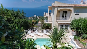 A pool area with lounge chairs, surrounded by lush greenery and a view of the sea. - CASA ANGELICA LUXURY VILLA (Priora)