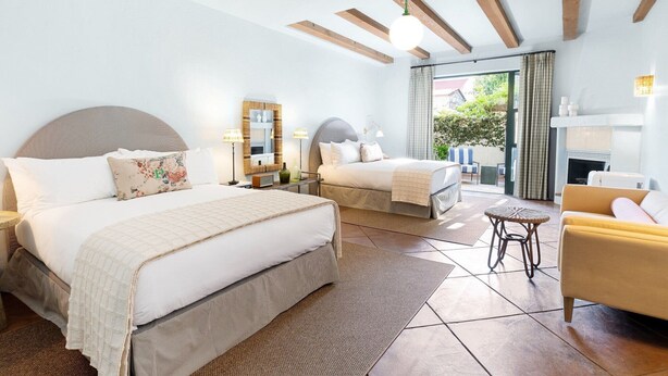 A hotel room with two beds, a sofa, a small table, a mirror, and a view of the outdoors. - Palihouse Santa Barbara (Santa Barbara)