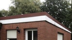 Una pequeña casa de ladrillo de un solo piso, con puerta frontal blanca, dos ventanas con contraventanas y un pequeño porche.