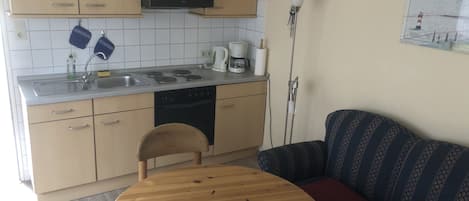 A compact kitchen with a sink, stove, and a dining area with a round table and a sofa.