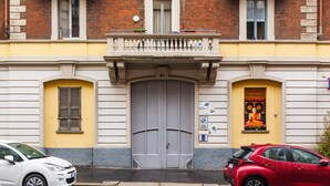 Ein Gebäude mit einer großen Zwerchhaustür, zwei Fenstern im Obergeschoss und einem kleinen Balkon mit Geländern.