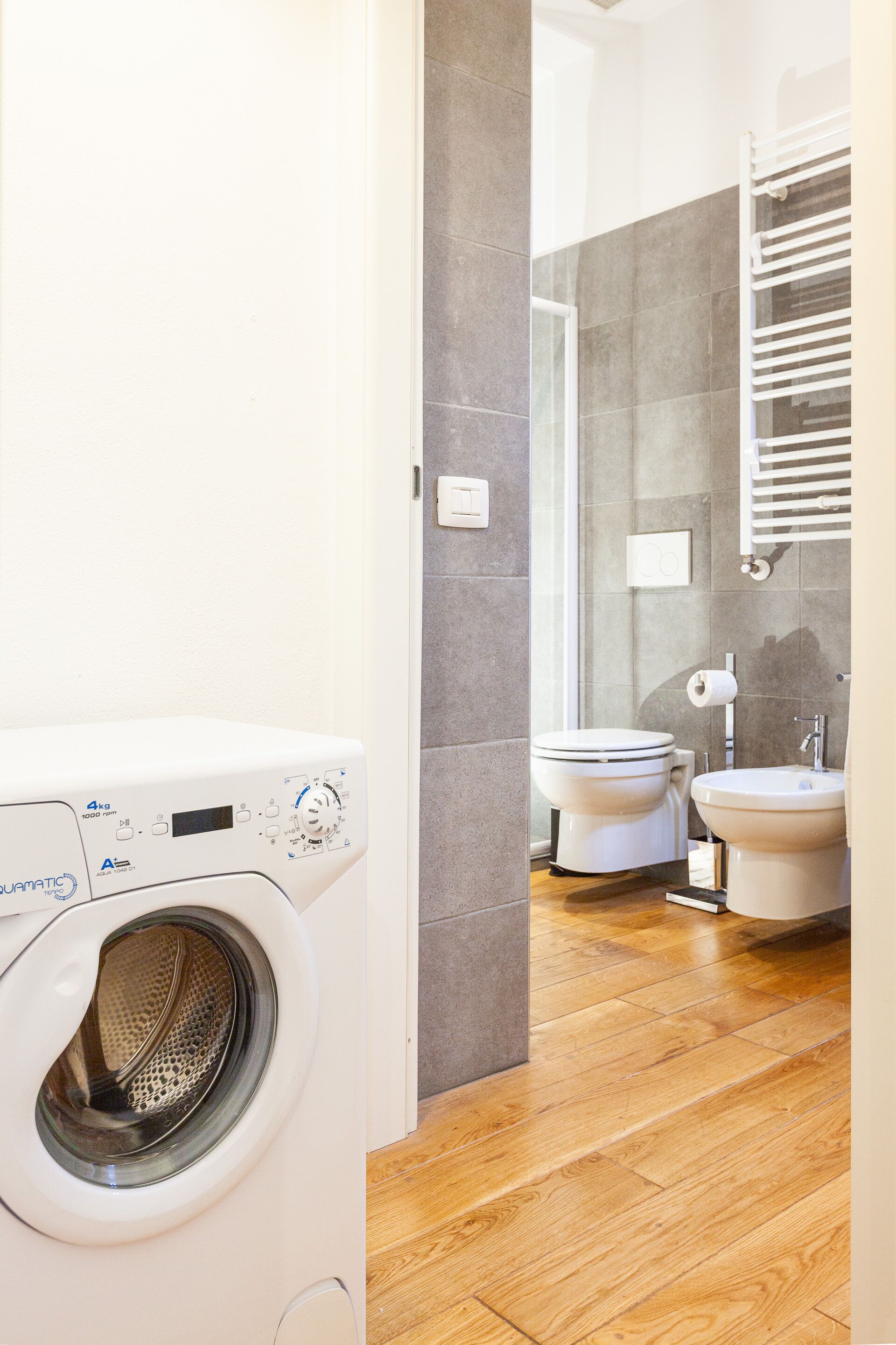 A modern bathroom with a washing machine, toilet, and sink.